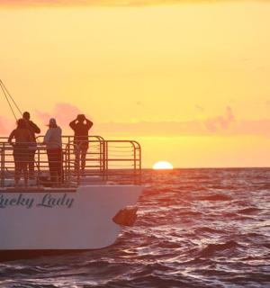 skupina lidí stojící na palubě lodi při západu slunce
