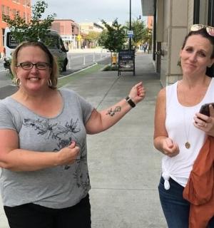 two women standing on a sidewalk with a cell phone