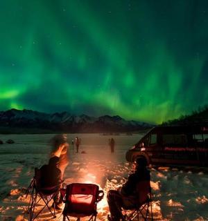 a group of people sitting around a camp fire under the aurora