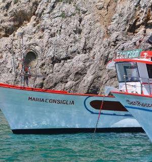 two boats sitting in the water next to a cliff