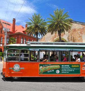 an orange trolley full of people riding on the street