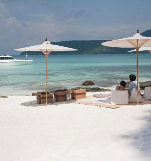 two people sitting under umbrellas on a beach with a boat