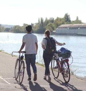 a man and a woman walking their bikes by the water