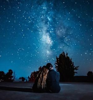 pár sedící na zemi a dívající se na hvězdy