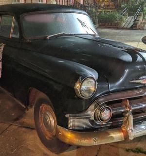 an old black car is parked on a sidewalk