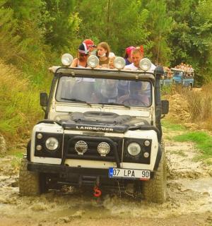 一群人坐在吉普车的后座上，行驶在一条土路上