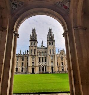 an archway leading to a large building with a green lawn