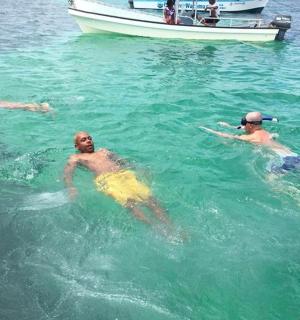 three men swimming in the water with a boat