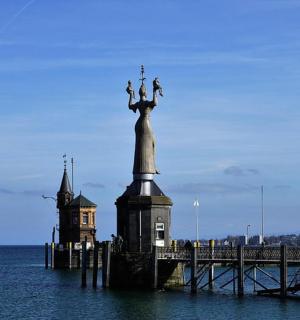 a statue in the middle of the water next to a pier