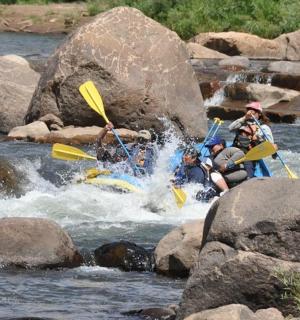 skupina lidí sjíždějících řeku s kameny na raftech