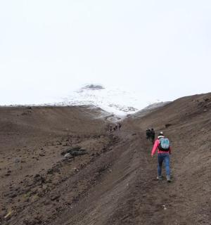 a man walking down a dirt road with a snow covered hill
