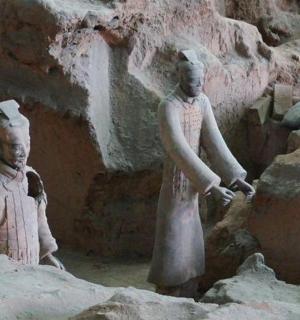 two statues of people standing next to a rock wall