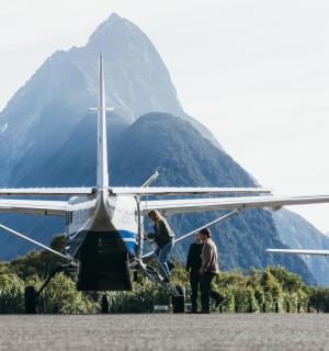两个人站在一架小型飞机旁,背景是一座山
