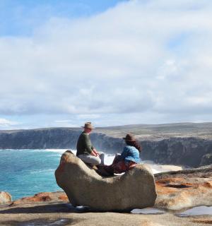 two people sitting on a rock overlooking the ocean