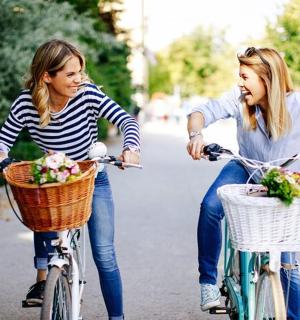 dvě dívky jedoucí na kolech s květinami v koších