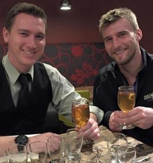 两个男人坐在桌边，手里拿着啤酒杯