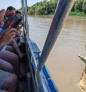 a crocodile standing in the water next to people on a boat