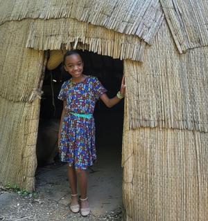 a young girl standing in a thatch hut