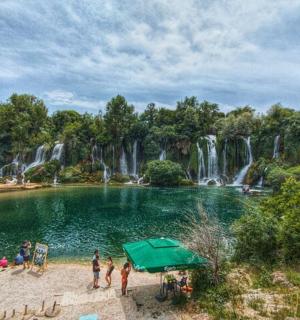 Skupina lidí stojících kolem rybníka před vodopádem