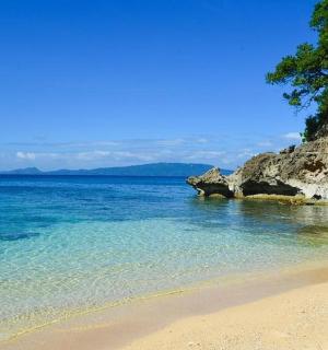 a beach with clear blue water and a cliff