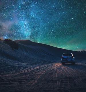 a car driving down a dirt road under a starry sky