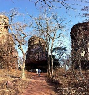 a person walking down a dirt road next to two large rocks