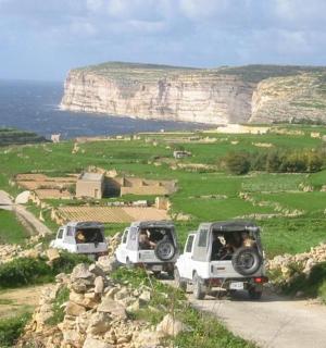 Dva bílé kamiony zaparkované na prašné cestě poblíž oceánu