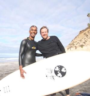two men standing on the beach holding a surfboard