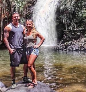 a man and woman standing on a rock in front of a waterfall