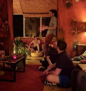 एक कमरे में बैठे लोगों का एक समूह और दीवार पर एक आदमी खड़ा है