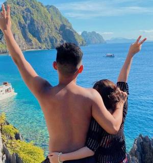 a man and a woman sitting on a cliff with their arms up