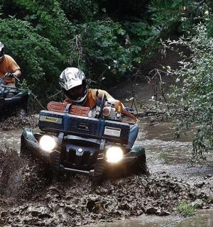 two people riding on atvs in the mud