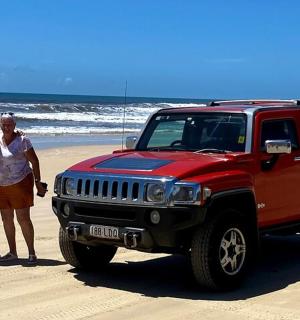a man and woman standing next to a red jeep on the beach