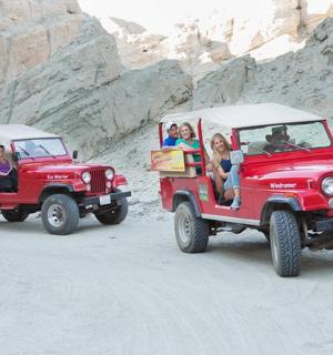 两辆红色吉普尼，载着乘客在沙漠中穿行