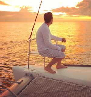 muž sedící na přídi lodi a pozorující západ slunce