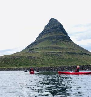 two people in red boats in the water with a mountain