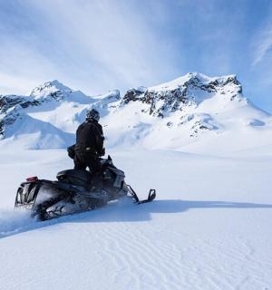 muž jedoucí na sněžném skútru ze zasněžené hory