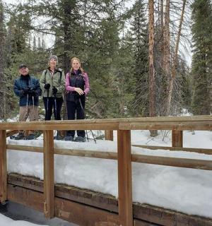 three people standing on a bridge in the snow