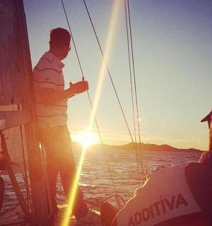a man standing on the side of a boat at sunset