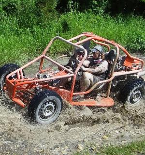dva lidé jedoucí v oranžovém čtyřkolovém voze v bahně