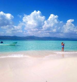 一名女子站在海滩上，水中有一条船