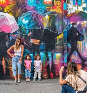 žena a dvě děti stojící před zdí s deštníky