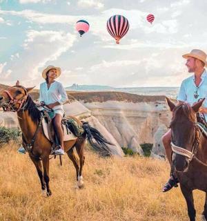 a couple riding horses in the grand canyon with hot air balloons
