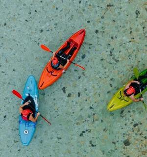 Skupina tří lidí v kajacích na pláži