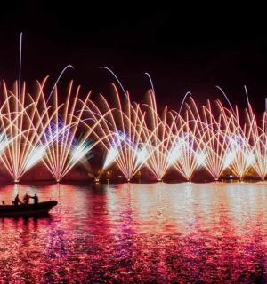 Skupina lidí v lodi ve vodě s ohňostrojem