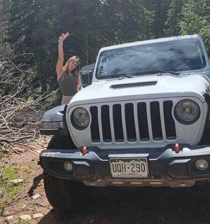 a woman standing on a jeep on a dirt road