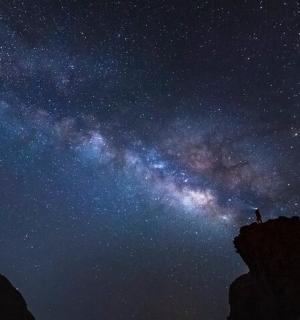 a starry sky with a person standing on a mountain