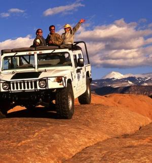 three people sitting on top of a jeep on a mountain