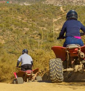 two people riding on atvs on a dirt road