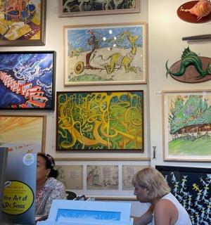 dvě ženy sedící u stolu v místnosti s obrazy